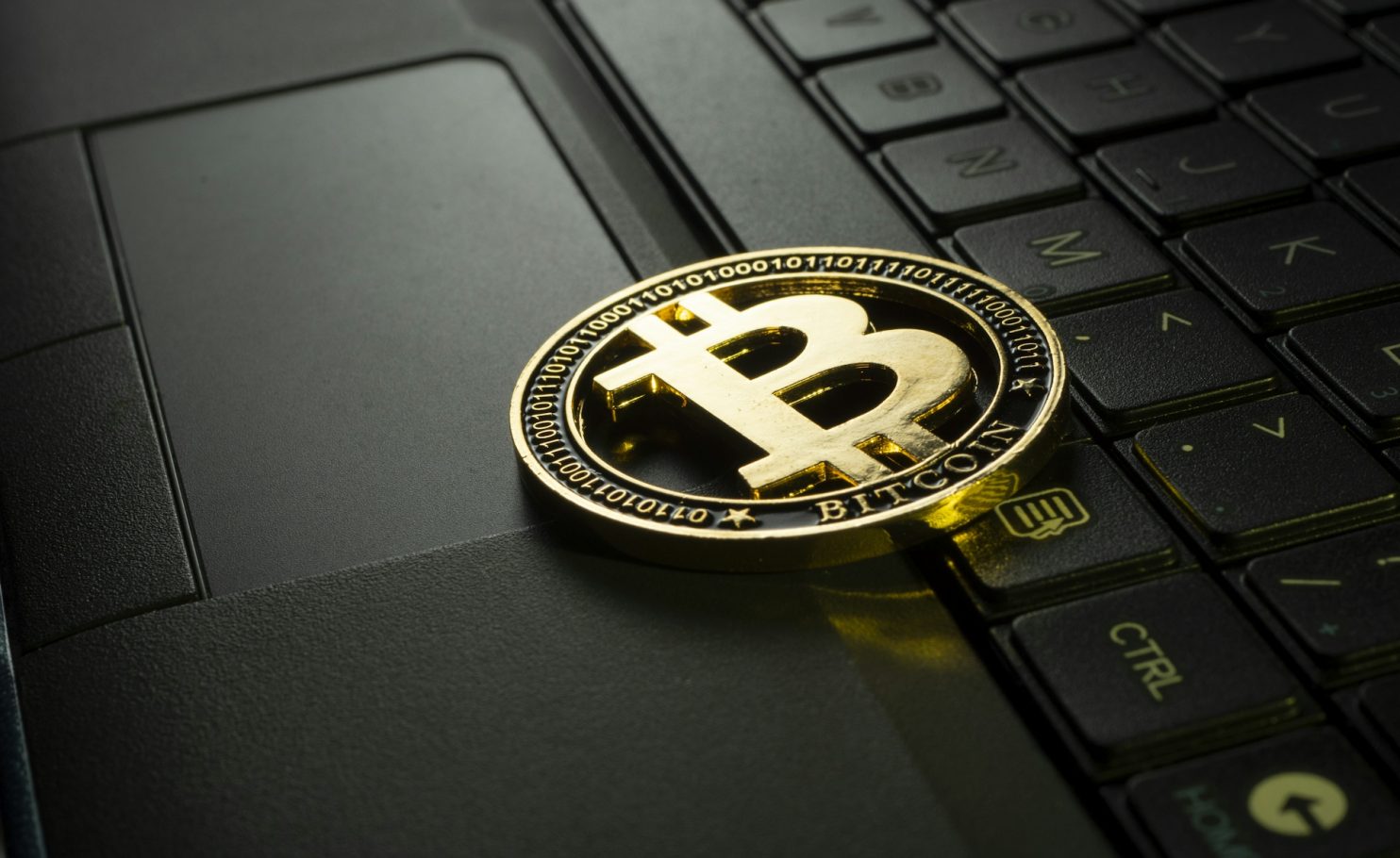 Bitcoin und Co Goldene Bitcoin-Münze liegt auf einer Laptop-Tastatur.